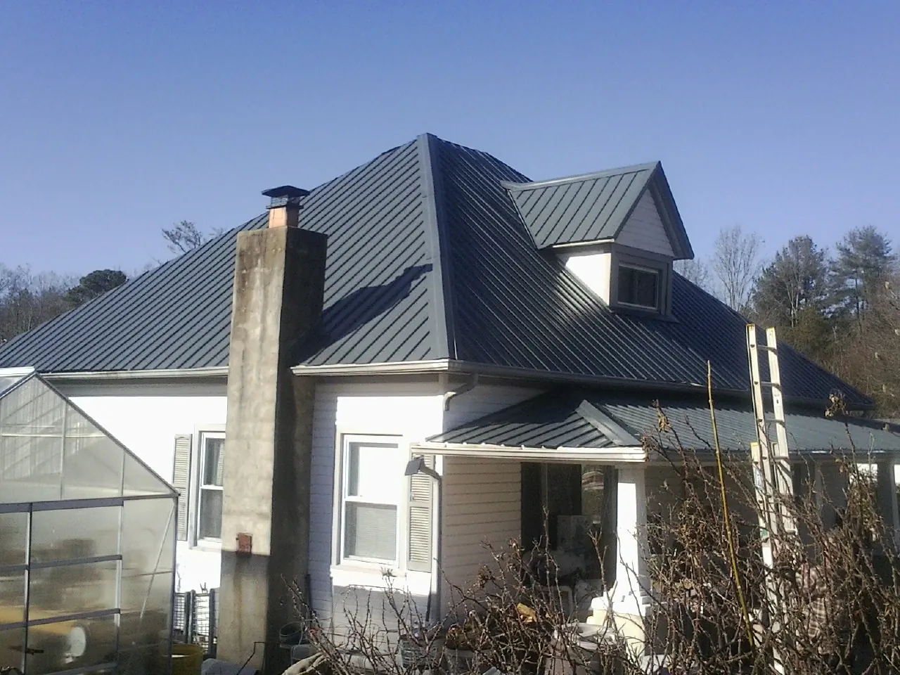 Dark blue standing seam metal roof on a white farmhouse with dormer — Slate & Tile Roof Repair by Roofing Brothers in Evansdale