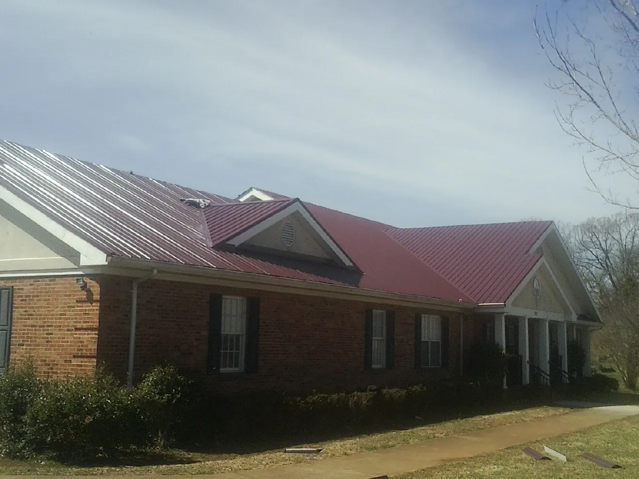 Red metal roof with gabled entries on a long brick building, from a Hail Damage Roof Repair job in Evansdale