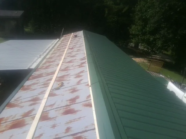 Old rusted panels beside newly installed green metal roofing — Wind Damage Roof Repair by Roofing Brothers in Evansdale