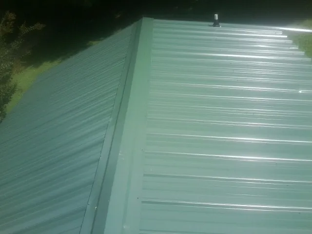 New green metal panels meeting at the ridge of a roof — Flat Roof Repair work by our crew in Evansdale