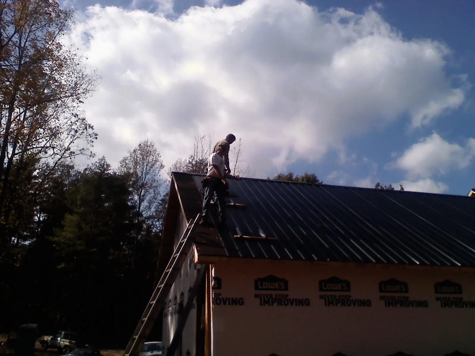 Roofer fastening dark metal panels high against a cloudy sky, from a Roof Inspection job in Evansdale