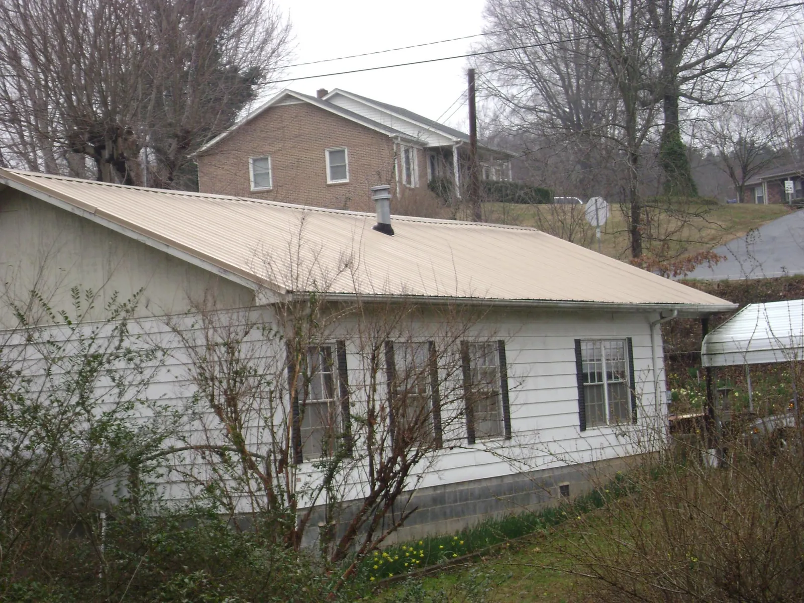 Tan metal roof on a white sided house set into a hillside — Commercial Roofing by Roofing Brothers in Evansdale