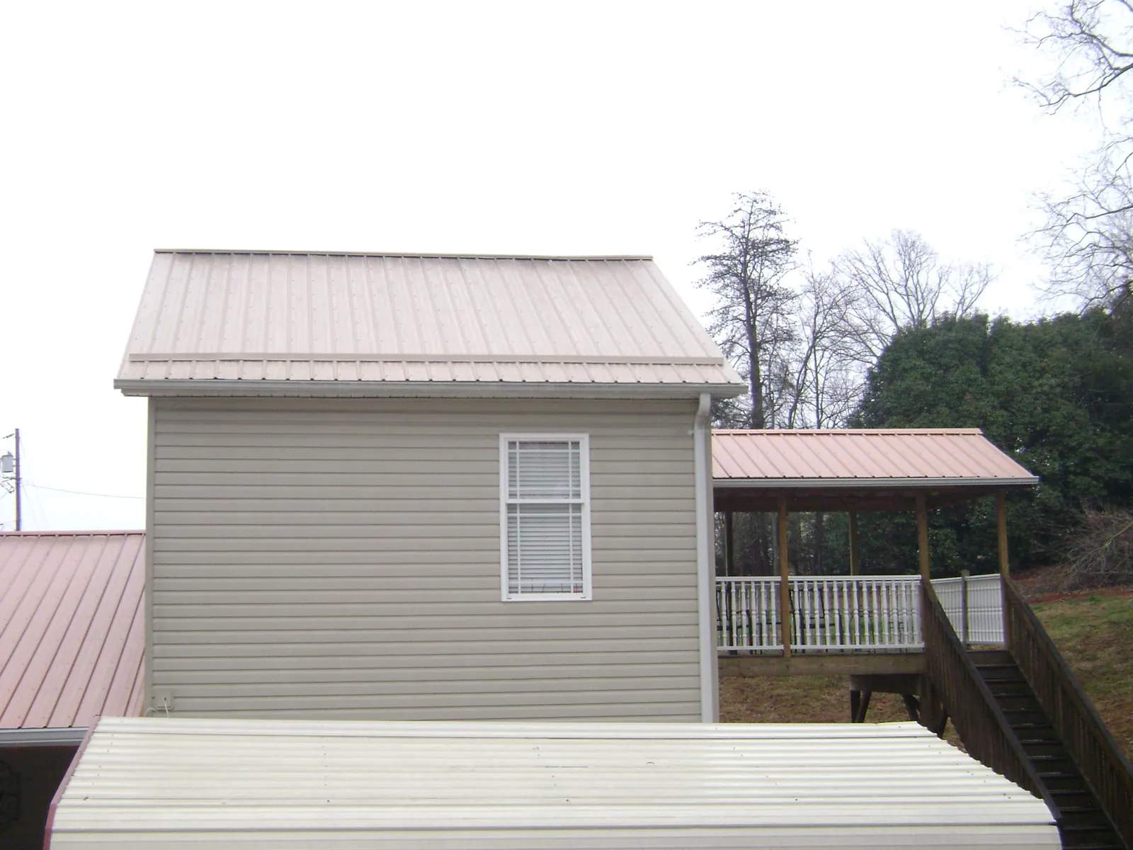 Tan metal roofs on a two story addition and attached porch, from a Roof Replacement job in Evansdale
